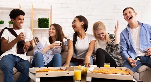 Happy teens eating pizza at home party, talking and laughing, panorama